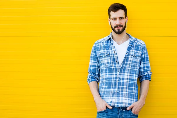 Jovem homem bonito com fones de ouvido na parede amarela — Fotografia de Stock