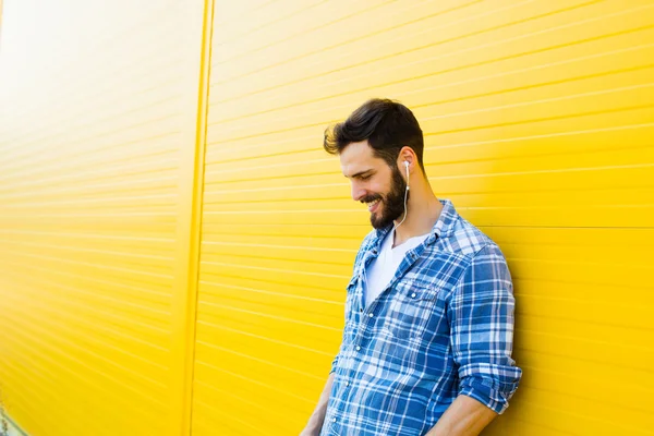 Jeune homme beau avec écouteurs sur le mur jaune — Photo