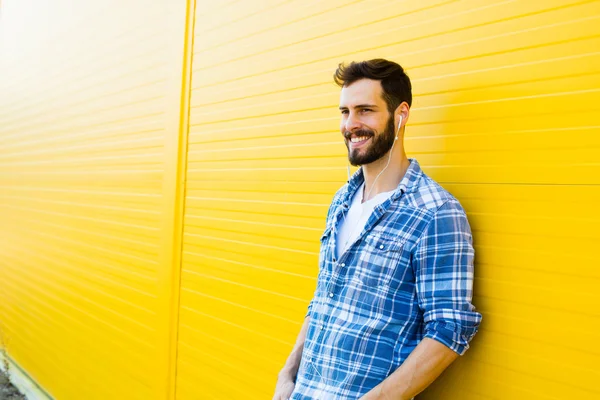 Junger schöner Mann mit Kopfhörern an gelber Wand — Stockfoto