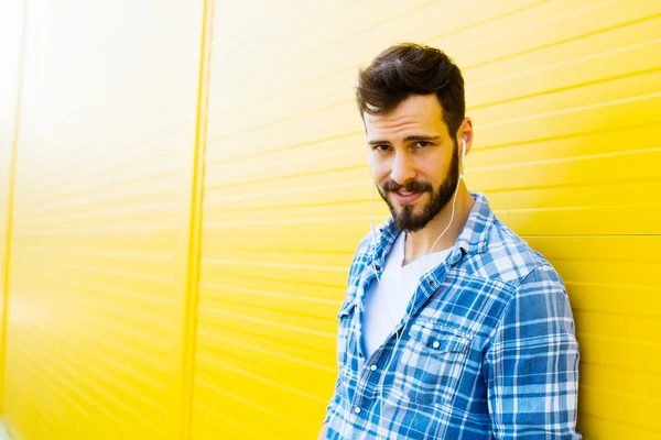 Молодой красивый мужчина с наушниками на желтой стене — стоковое фото