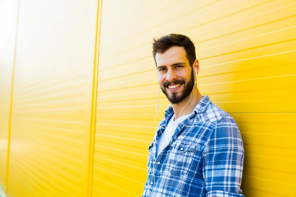 Joven hombre guapo con auriculares en la pared amarilla — Foto de Stock