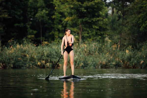 Vrouw doen opstaan peddel op een meer omringd door bomen — Stockfoto