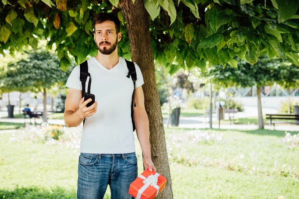 Homem com mochila e um presente ao lado de uma árvore — Fotografia de Stock