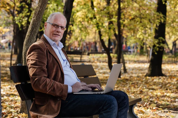 Vecchi uomini d'affari che lavorano al computer portatile fuori su una panchina — Foto Stock