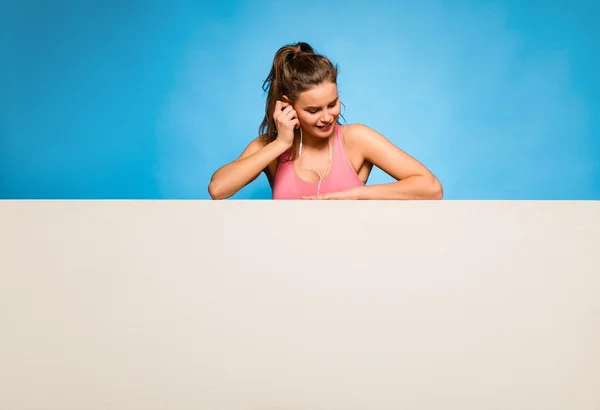 Mulher bonita com fones de ouvido sobre um painel vazio — Fotografia de Stock