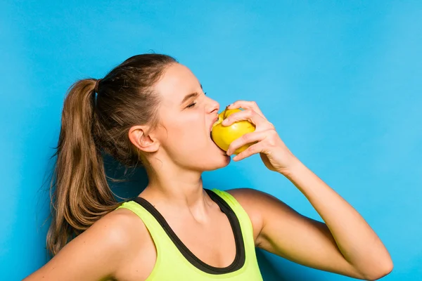 Pretty woman in sport equipment eating an apple in hand — Stock Photo, Image