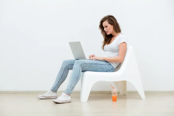 Alleinstehende Frau sitzt auf weißem Stuhl mit Laptop — Stockfoto