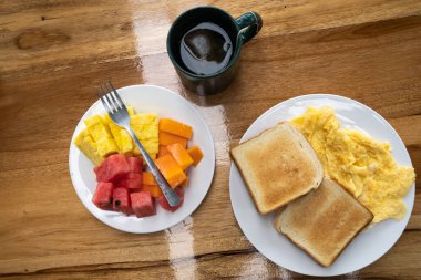 Meyve, çay ve yumurtalı ekmek ile birlikte ahşap bir masada servis edilen Avrupa kahvaltısının havadan çekilmiş fotoğrafı.