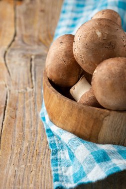 Portobello mantarlarının ahşap kasede, mavi kumaş üzerinde kırsal ahşap masa üzerinde, dikey, fotokopi alanı ile