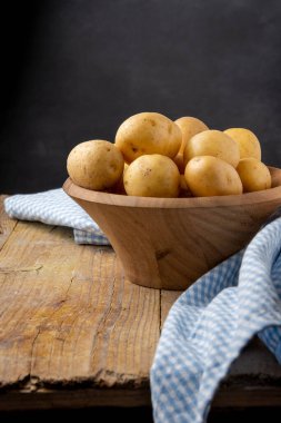 Tahta kasede küçük sarı patatesler, seçici bir odak, mavi kareli kumaş, kırsal ahşap masa, ve siyah arka plan, dikey olarak, kopyalama alanı ile