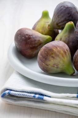 Beyaz bir plaka üzerinde mor incir yakın plan, seçici odaklı, bez ve beyaz ahşap masa, dikey