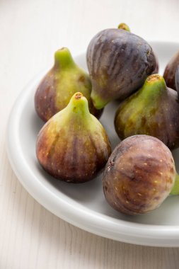 Beyaz tahta masada beyaz bir tabakta incir üst görünümü, seçici odaklı, dikey