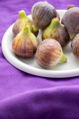 Mor battaniyede beyaz bir tabakta incir üst görünümü, seçici odaklı, dikey