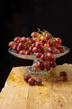 Kırmızı üzümlü cam meyve kasesinin üst görüntüsü, seçici odak, tahta masa, dikey siyah arkaplan