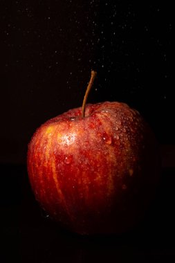 Düşen su damlaları ile kırmızı elmanın görüntüsü, seçici odaklı, siyah arkaplan, dikey, kopyalama alanı ile aydınlatılmış
