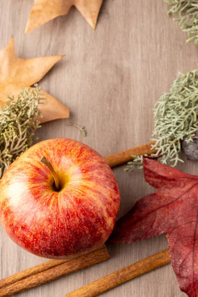 Aerial view of a royal gala apple with cinnamon sticks and autumn leaves, selective focus, on wooden table, vertical, with copy space