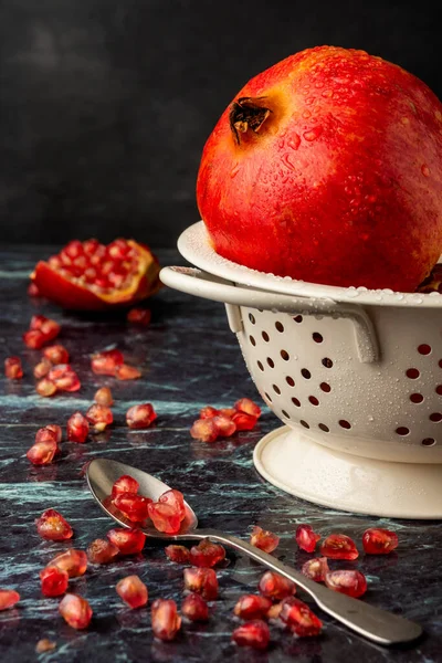 Nar tohumlu kaşık yakın plan, ıslak kırmızı nar ve tohumlu beyaz süzgeç, seçici odaklı, mavi mermer, ve dikey arkaplan,