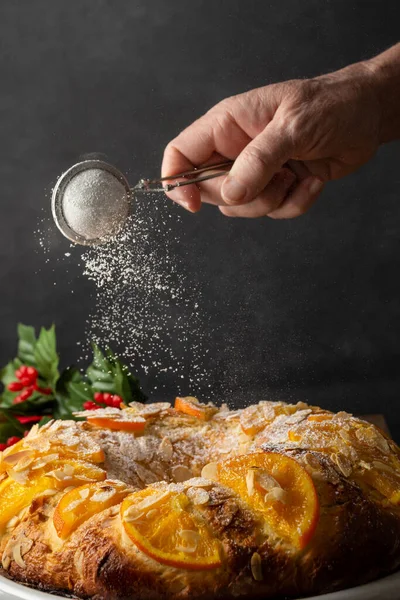 Kadının elinin, ev yapımı Roscon de Reyes 'e şeker dökerken yakın plan, koyu arka plan, dikey