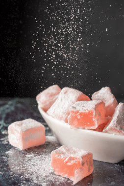 Beyaz kasede güllerle Türk Lokumu 'nun üst görüntüsü, mavi mermer üzerine düşen şeker, seçici odak ve siyah arka plan, dikey