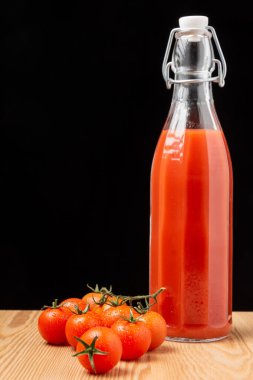 Ahşap masada domates suyu ve kiraz domatesli cam şişe manzarası, siyah arkaplan, dikey, fotokopi alanı