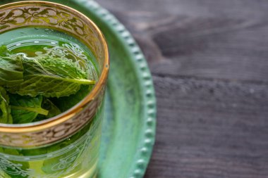Kırsal ahşap masa üzerinde, yatay olarak fotokopi alanı olan yeşil tabakta, arap çay ve nane şekeri ile yakın plan.