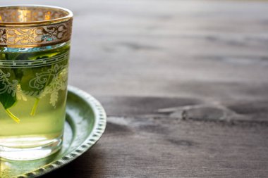 Yeşil tabakta naneli, yarı dekore edilmiş çay bardağının yakın çekimi ve koyu ahşap masa, yatay ve fotokopi alanı var.