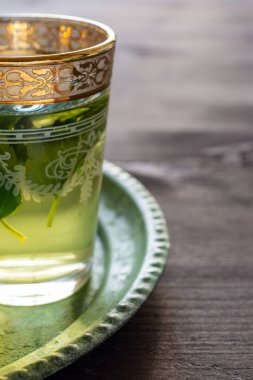 Yarı dekore edilmiş, yeşil tabakta naneli çay bardağı ve koyu ahşap masa, dikey olarak, kopyalama alanı ile.