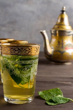 Süslü çay bardaklarını yakın plan, koyu ahşap masa üzerinde nane, arka planda çaydanlık, dikey, kopyalama alanı ile