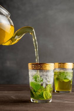 Naneli çay servisi yapan çaydanlık manzarası, iki süslemeli bardak, seçici odak, ahşap masa, gri arka plan, dikey, kopyalama alanı olan