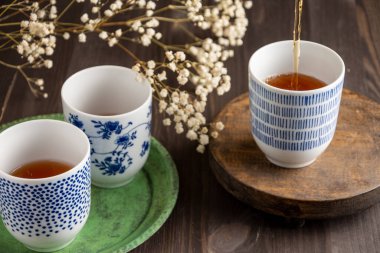 Üç mavi fincanın görüntüsü çay, beyaz çiçekler, seçici odak, yeşil tabak ve tahta masa, yatay