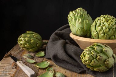 Tahta kasedeki yeşil enginarların üst görüntüsü siyah bez ve bıçaklı, seçici odaklı, tahta masa, siyah arka plan, yatay