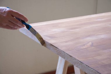 Çam ağacından bir masanın üzerinde fırçayla uzanan kadın eli manzarası, yatay.