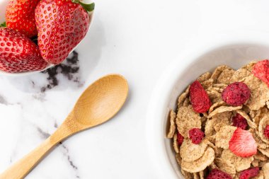 Mısır gevreği, kırmızı böğürtlen, çilekli kase ve ahşap kaşık, beyaz mermer masa üzerinde, yatay olarak, fotokopi alanı ile.