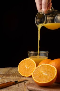 Portakallı, siyah arka planlı, portakallı, portakal suyu dolu bir sürahi ile portakal suyu servis eden bir kadın eli görüntüsü