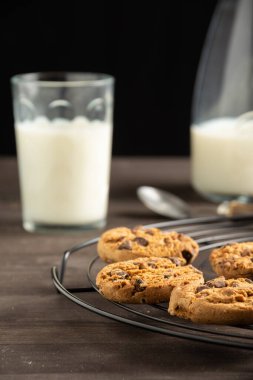 Tel raftaki kurabiyelerin yakın çekimi, cam ve süt şişeli ahşap masa, seçici odak, siyah arka plan, dikey