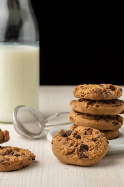 Beyaz tabakta çikolatalı kurabiyelerin ve sütlü şişenin yakın plan resmi, beyaz masa, siyah arkaplan, dikey, kopyalama alanı