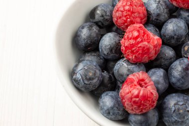Beyaz kâse, beyaz böğürtlenli ve ahududulu, beyaz masa üzerinde, yatay ve fotokopi alanı olan.