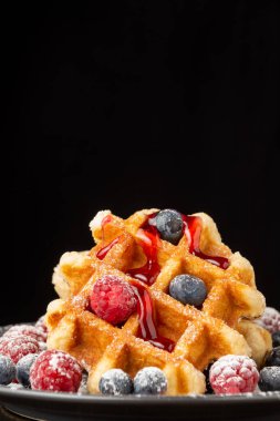 Çilekli böğürtlen ve yaban mersinli waffle yakın plan, siyah arkaplan, dikey, kopyalama alanı ile