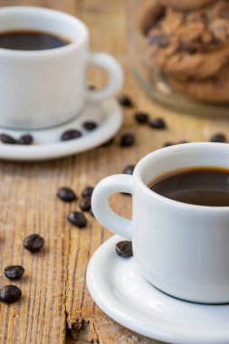 Top view of white cups of coffee, on rustic wooden table with coffee beans and jar with cookies, selective focus, vertical