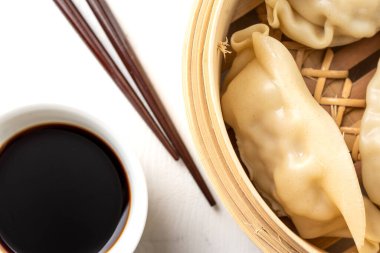 Gyozalı buharlı hava manzarası, soya soslu kase ve yemek çubukları, beyaz ahşap, yatay.