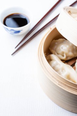 Gyozalı açık buharlı vapurun üst görüntüsü, kasede soya sosu ve yemek çubukları, beyaz ahşap üzerinde, dikey, kopyalama alanı ile.