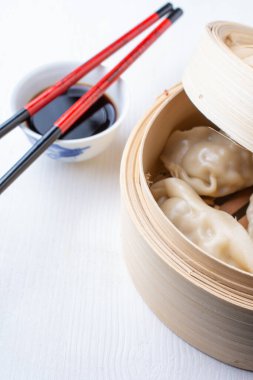Gyozalı açık buharlı vapurun üst görüntüsü, yemek çubuklarıyla soya sosu, beyaz ahşap, dikey, kopyalama alanı olan.