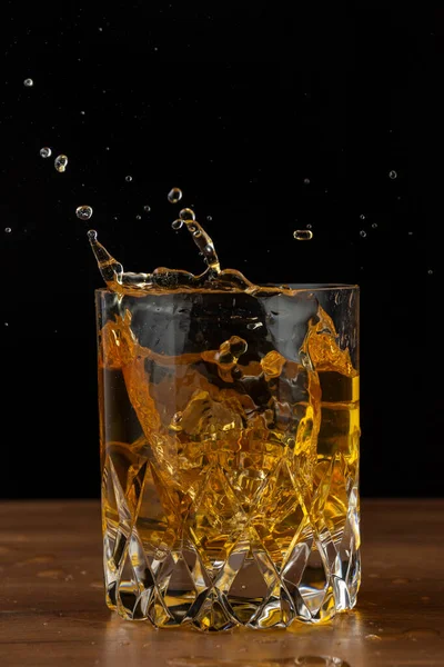 Szkło Kryształowe Rozpryskiem Whisky Drewnianym Stole Czarnym Tle Pionie Przestrzenią — Zdjęcie stockowe