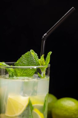 Buzlu, limonlu, limonlu, siyah pipetli ve nane yapraklı, siyah arkaplanlı mojito kokteyli.