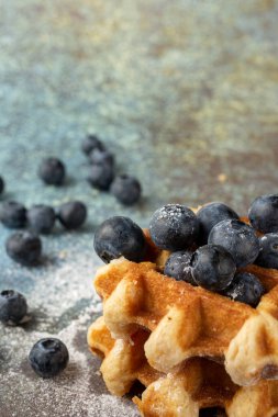 Yaban mersinli ve şekerli waffleların üst görüntüsü, mavi arkaplanda yaban mersinli, seçici odak, dikey, kopyalama alanı ile