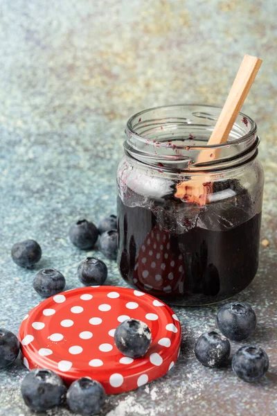 玻璃瓶与蓝莓果酱和木制勺子的特写 蓝色背景与蓝莓和波尔卡圆点盖 选择焦点 — 图库照片