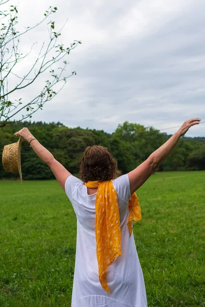 Arkadan beyaz giyinmiş, kolları havada, odaklanmamış yeşil alan arkaplanı olan, portrede, fotokopi alanı olan olgun bir kadın görüntüsü