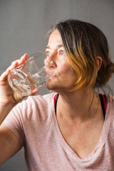 Spor yaptıktan sonra portrede bardaktan su içen olgun bir kadının yakın çekimi.