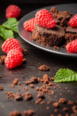 Koyu tabakların üst görüntüsü ahududu ve nane yapraklı browni parçaları, seçici odaklı, kırıntıları olan koyu masa, dikey