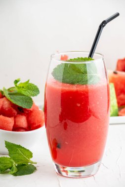 Karpuz suyu, kamış, nane ve karpuz parçalarıyla dolu bir bardağın üst görüntüsü, masa ve beyaz arka planda, dikey olarak seçici odak.